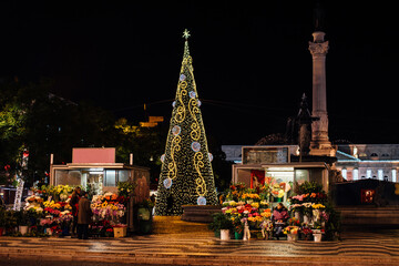 Illuminated Christmas tree and flower shops in Lisbon's square during festive Christmas time at...