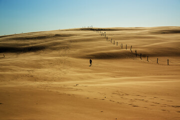 Krajobraz pustynny błękitne niebo i ruchome piaski z sylwetką idącego człowieka w pięknym świetle zachodzącego słońca	
