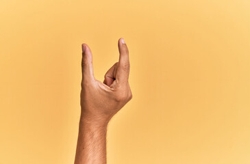 Arm and hand of caucasian man over yellow isolated background picking and taking invisible thing, holding object with fingers showing space