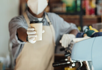 Young african american barista in protective mask and gloves holds paper cup with hot drink in hand