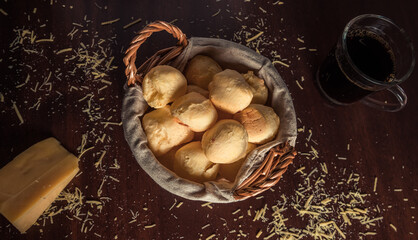 Cheese bread 'pao de queijo' basket with slice of cheese, and grated cheese on rustic wooden table. Top View