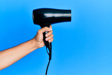 Hand of hispanic man holding hair dryer over isolated blue background.