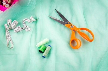 Scissors tailor and inch, centimeter tape and green threads on a background of  green tulle fabric. Tailor's equipment. Sewing tools.