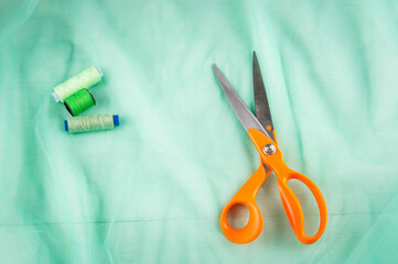 Scissors tailor and inch, centimeter tape and green threads on a background of  green tulle fabric....