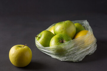single use plastic packaging issue. green apples in plastic bags  on a dark background