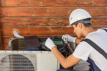 A young electrician repairs an air conditioner. Split system maintenance