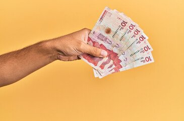 Hand of hispanic man holding colombian 10 pesos banknotes over isolated yellow background.