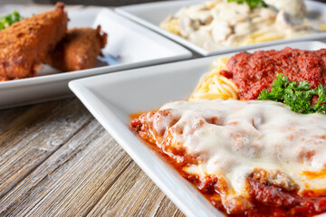 A view of several Italian entrees on a wooden table surface, featuring chicken parmigiana.