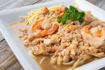A view of a rustic plate of seafood spaghetti, featuring shrimp and clam meat.