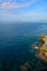 Barca a vela in rada fuori dal poro di Camogli osservata dalla scogliera (Liguria, Italia)