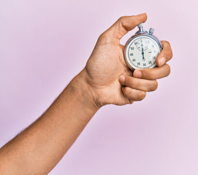 Hand of young hispanic man using stopwatch over isolated pink background.