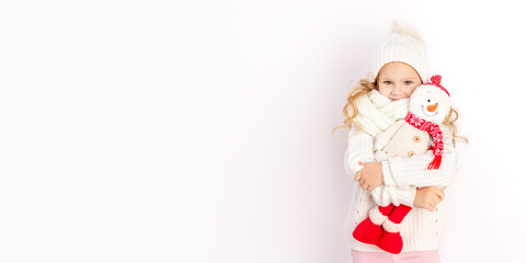 Fototapeta premium baby girl with snowman toy in warm hat and sweater on white isolated background, place for text, banner