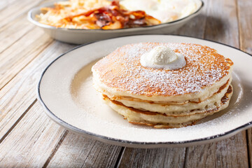 A view of a stack of pancakes next to a breakfast plate.
