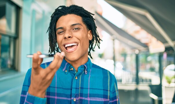 Young african american man sending audio message using smartphone at street of city.