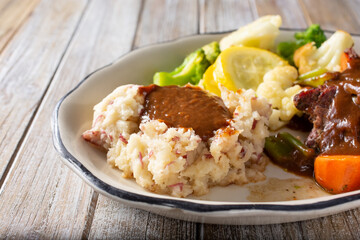A view of a side of mashed potatoes, topped with gravy, part of a pot roast entree.