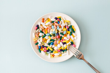 Creative medical layout made with colorful pills, capsules and supplements on white plate on light blue background. Minimal modern pharmacy or health care concept. Flat lay, top view, copy space