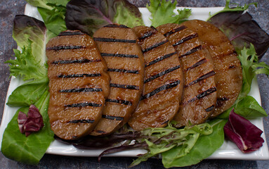 Grilled seitan slices glazed with raspberry chipotle sauce, on a bed of greens, copy space