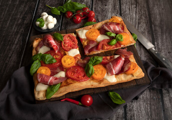 Italian rectangular pizza with tomatoes, mozzarella and briazolla on a wooden table.