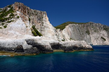 Limestone rocks on the coast of Zakynthos island, Greece. Sunny day, crystal clear water, blue sky, boat trip, rocks falling steeply into the sea.