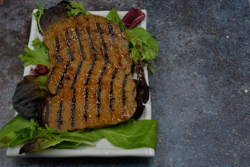 Grilled seitan slices glazed with raspberry chipotle sauce, on a bed of greens, copy space