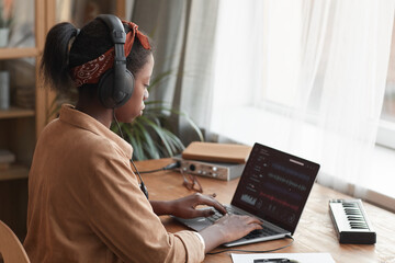 Side view portrait of female African-American musician using laptop with sound editing software...