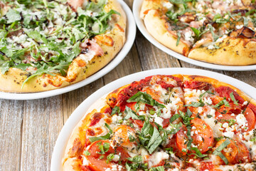 A view of several rustic pizzas on a wooden table surface.