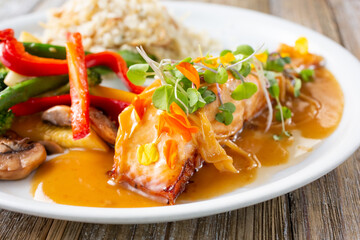 A view of a plate of seared salmon filet, featuring sides of grilled veggies and rice pilaf.