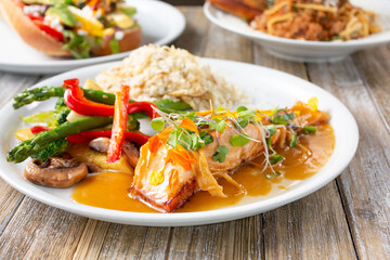 A view of a several gourmet entrees on a wooden table surface, featuring a plate of seared salmon filet.