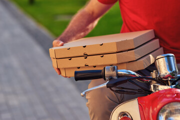 Courier in red uniform sitting on scooter and holding pizza boxes