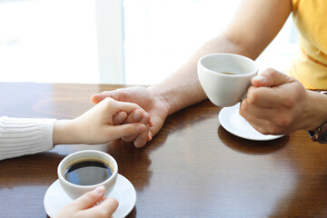 Female and man hands with cups of coffee on the background of a wooden table. Relationship concept during travel vacation. Focus on together hands