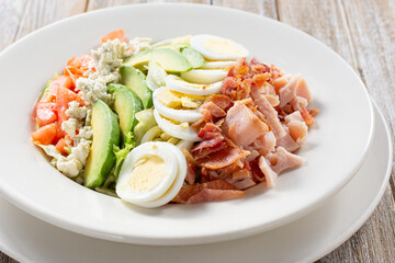A view of a plate of cobb salad, in a restaurant or kitchen setting.