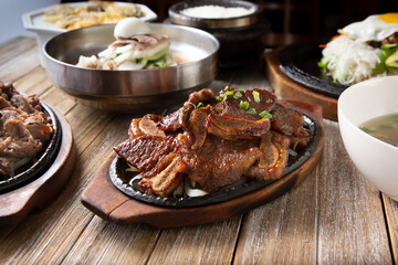 A view of several Korean entrees prepared on a wooden table surface, featuring galbi.