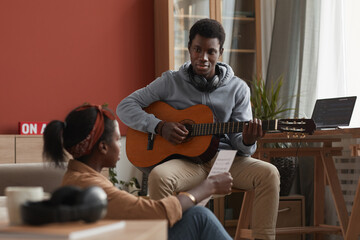 Portrait of two young African-American musicians playing guitar and writing music together in home...