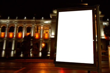 Blank signboard on the background of the night city. Mockup for design. Free space for advertising. Sharpness on the banner from the edge of the frame.