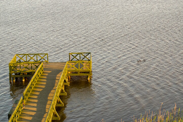 Żółty pomost na jeziorze z przepływającymi obok kaczkami
