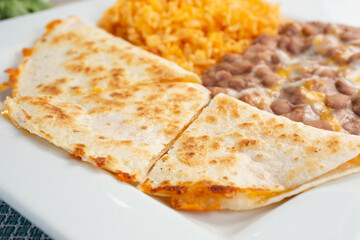A view of a plate featuring a quesadilla, rice and beans, in a restaurant or kitchen setting.