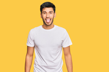 Young handsome man wearing casual white tshirt sticking tongue out happy with funny expression. emotion concept.