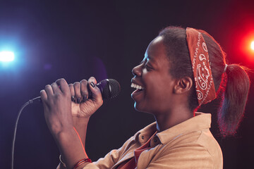 Side view portrait of young African-American woman singing to microphone while standing on stage