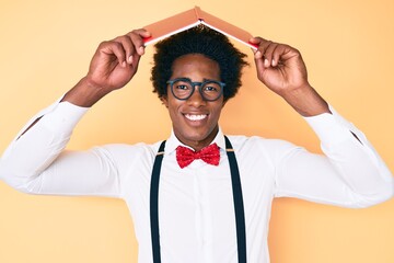 Handsome african american nerd man with afro hair holding book over head smiling with a happy and...