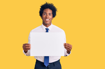 Handsome african american man with afro hair holding blank empty banner looking positive and happy standing and smiling with a confident smile showing teeth