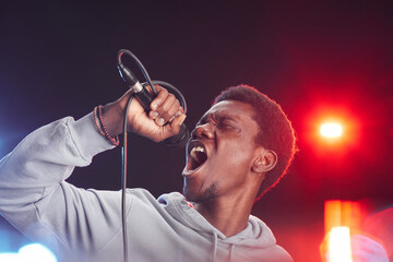 Portrait of young African-American man singing to microphone passionately while standing on stage...