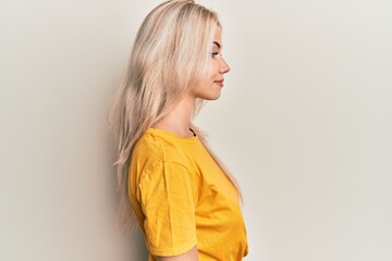 Beautiful caucasian blonde girl wearing casual tshirt looking to side, relax profile pose with natural face with confident smile.