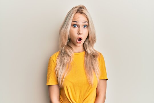 Beautiful caucasian blonde girl wearing casual tshirt afraid and shocked with surprise expression, fear and excited face.