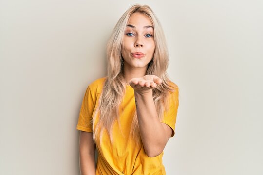 Beautiful caucasian blonde girl wearing casual tshirt looking at the camera blowing a kiss with hand on air being lovely and sexy. love expression.