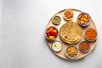 Indian Thali - selection of various dishes served on round wooden platter, white table. Assorted Indian vegetarian meze with chapati bread, paneer, dal, chutney in bowls. Top view, space for text