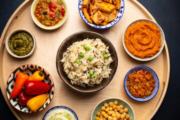 Indian Thali - selection of various dishes served on round wooden platter. Assorted Indian vegetarian meze with boiled basmati rice, paneer, dal, chutney in different bowls. Top view