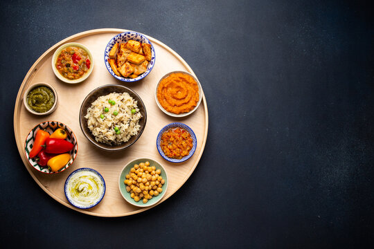 Indian Thali - selection of various dishes served on round wooden platter. Assorted Indian vegetarian meze with boiled basmati rice, paneer, dal, chutney in different bowls. Top view, space for text