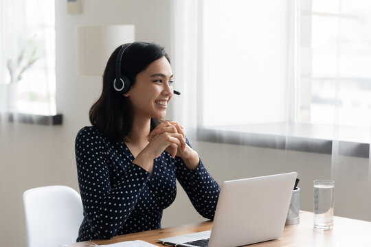 Smiling Asian Businesswoman Wearing Headset Using Laptop, Looking To Aside, Dreaming About New Job Opportunities, Happy Woman Student Watching Webinar, Listening To Lecture, Studying, Home Office