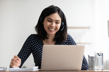 Close up smiling Asian woman wearing headset looking at laptop screen, student intern watching...