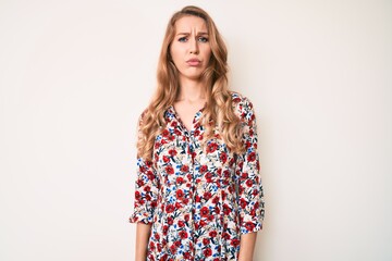 Young caucasian woman with blond hair wearing summer dress skeptic and nervous, frowning upset...